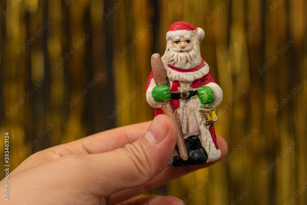 Obraz premium Woman hand holding a Santa Claus figurine on golden background. Christmas decoration