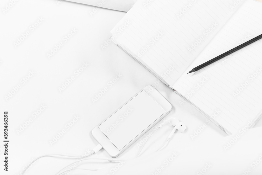 Naklejka premium Notebook, pencil, Smartphone, and earphones, on the bed, white sheets. White background, copy space, mockup.