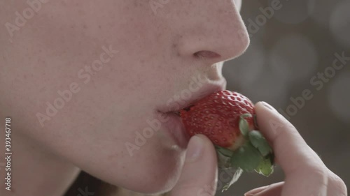 Close-up side view of european beautiful woman eating ripe delicious red strawberry in summer. Health and vegan food concept. Slow motion