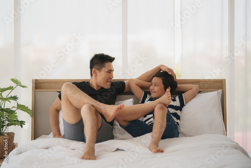 asian dad and son have good time talking together on bed at home