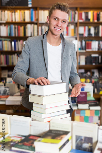 happy male student standing in library with pile of books in hands
