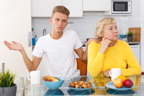 Young guy asking for forgiveness his offended mother at kitchen