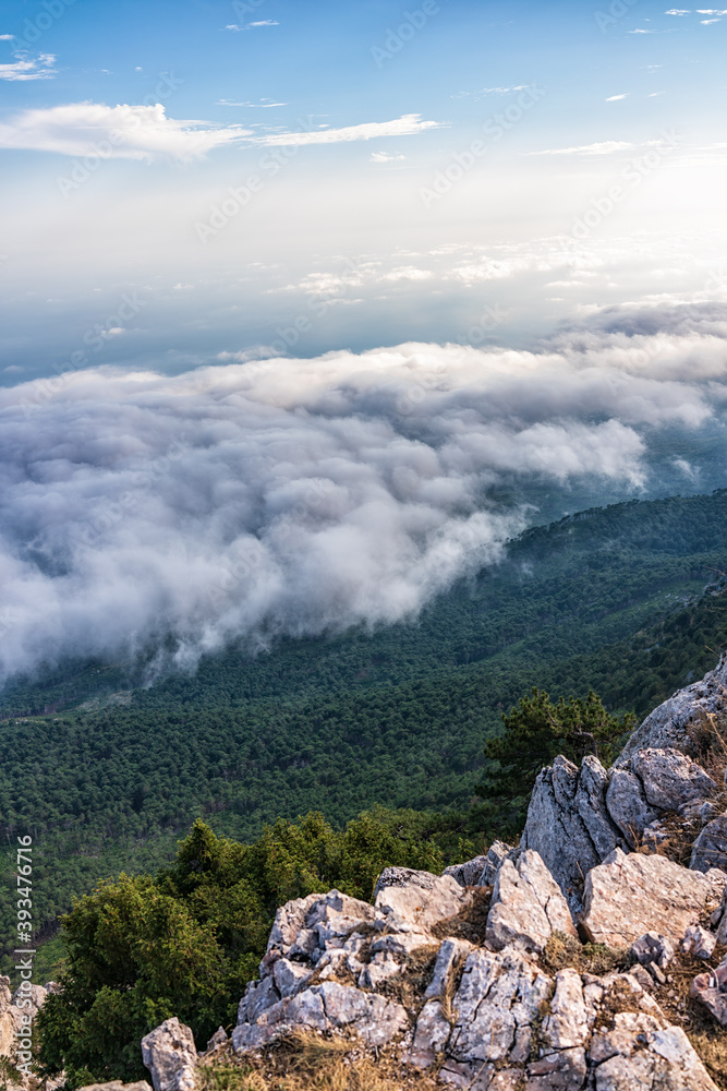 A majestic view of the rocky mountains and the valley in fog and clouds. Creamy fog covered the mountain valley in sunset light. Picturesque and gorgeous scene. Misty sunset over Crimea Mountains