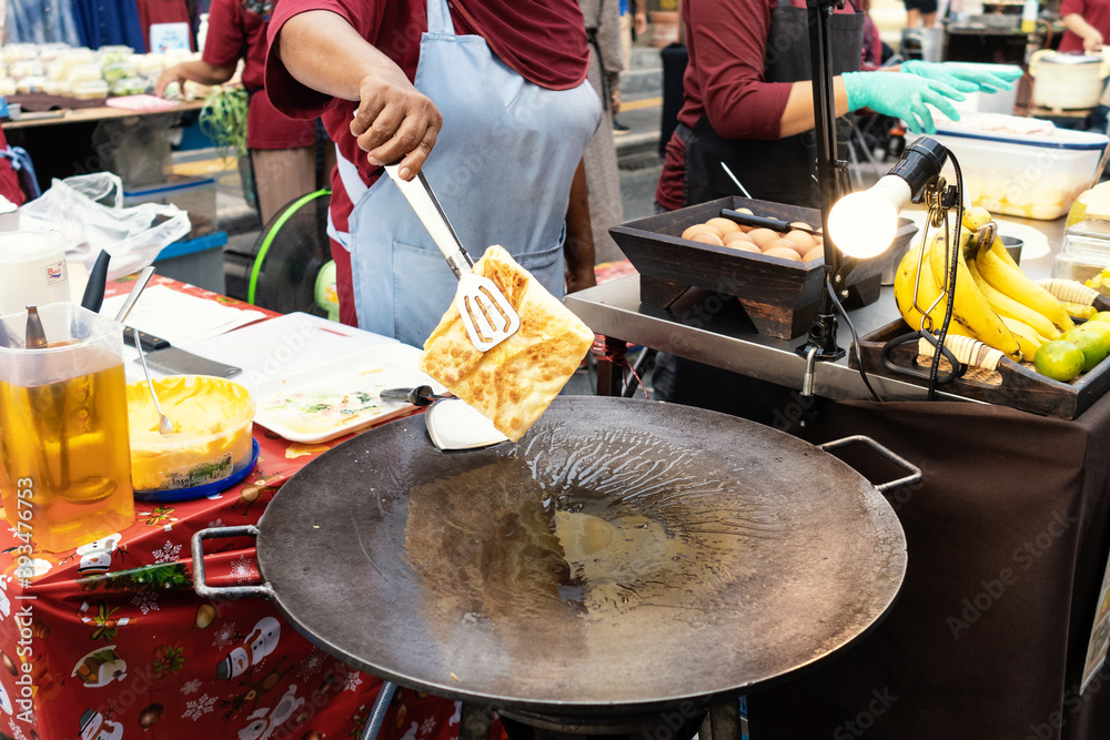 Fototapeta premium Thai woman is cooking banana pancake on pan with butter on the street.