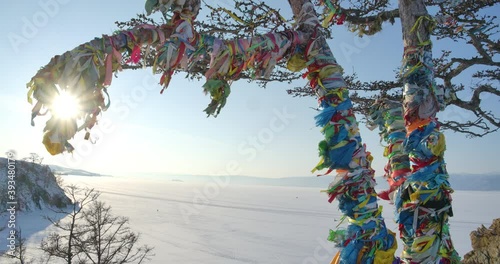 Colored ritual ribbons tied up on a shamanic tree with the frozen Lake Baikal background at Shaman rock in cape Burhan of the Olkhon Island, Russia. Slowmotion. photo
