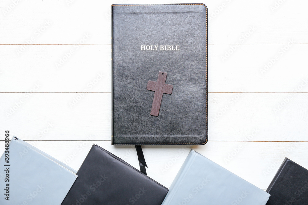 Holy Bible, books and cross on light wooden table