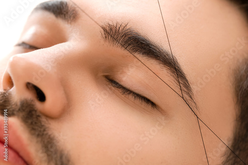 Young man undergoing eyebrow correction procedure in beauty salon, closeup photo