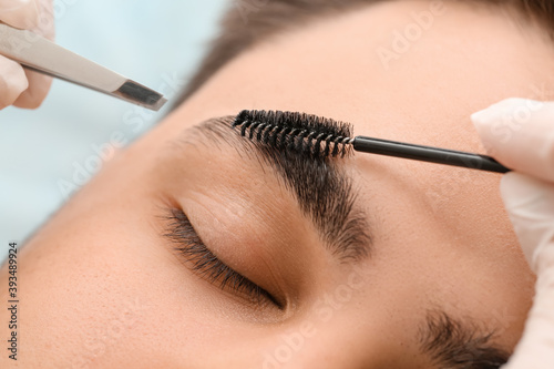 Young man undergoing eyebrow correction procedure in beauty salon, closeup photo
