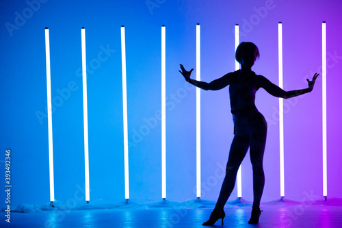 Graceful young woman dancing elements of modern dance in the studio on a blue purple background with neon lighting lamp. Dance poster design.