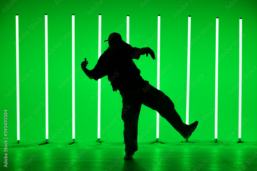 Silhouette of man giving solo performance in hip hop style on club scene with green background neon lamps. Close up. Dance school poster.