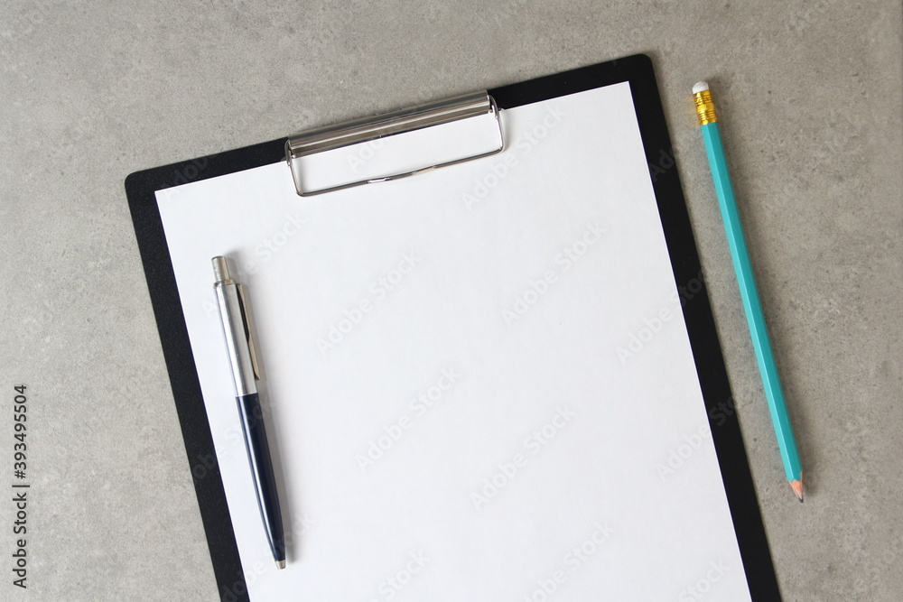 Template of white paper with a ballpoint pen and simple pencil on light grey concrete background in a black tablet with a clip. Concept of new idea, business plan and strategy, empty space for text Template of white paper with a ballpoint pen and simple pencil on light grey concrete background in a black tablet with a clip. Concept of new idea, business plan and strategy, empty space for text