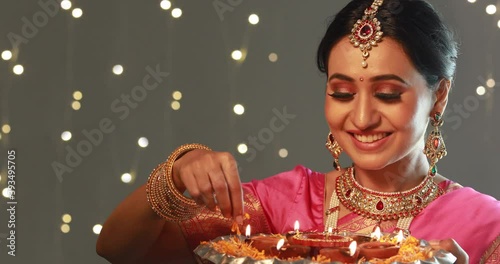 Woman in ethnic attire decorating a plate full of diyas with flowers	 photo