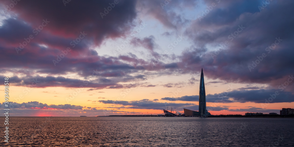Scenic evening view of a tall skyscraper by the sea. Beautiful sunset over the Baltic Sea. Dramatic clouds in the sky. Modern architecture and sights of St. Petersburg. Russia.