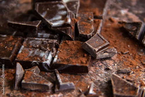 Dark chocolate bar with chocolate pieces with cocoa powder on brown background, close-up view