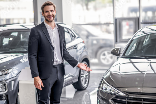 Brown-haired male standing in showroom, presenting new car © zinkevych