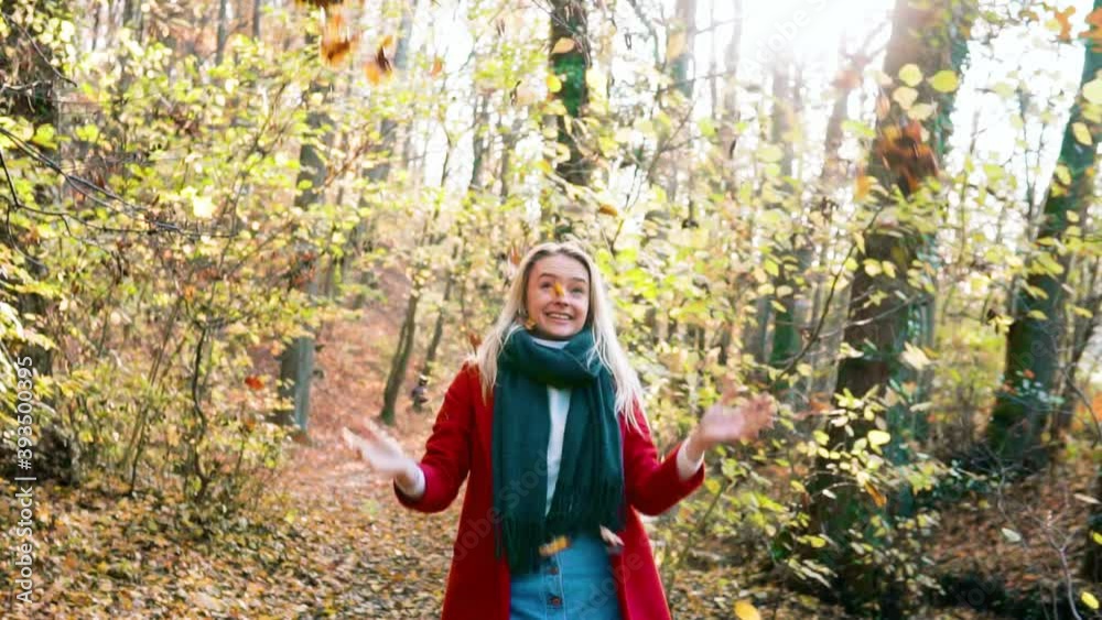 SLOWMOTION Young beautiful woman throwing leaves in the air amidst thee orange brown autumn forest woodland while wearing a red coat. Version 1 SLOWMOTION Young beautiful woman throwing leaves in the air amidst thee orange brown autumn forest woodland while wearing a red coat. Version 1