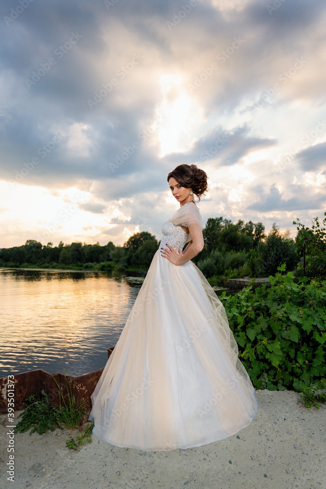 beautiful girl in a white wedding dress in summer by the river on a sunset background