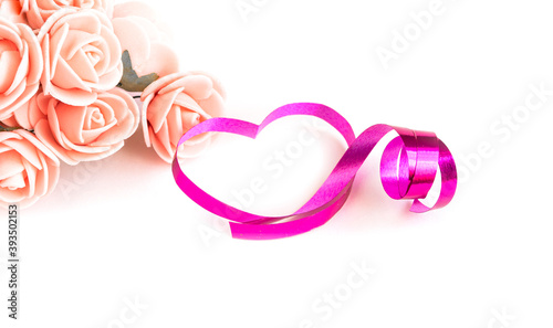 Pink gift ribbon in the shape of hearts and rose flowers on a white isolated background, Valentine's day concept. Copy space.