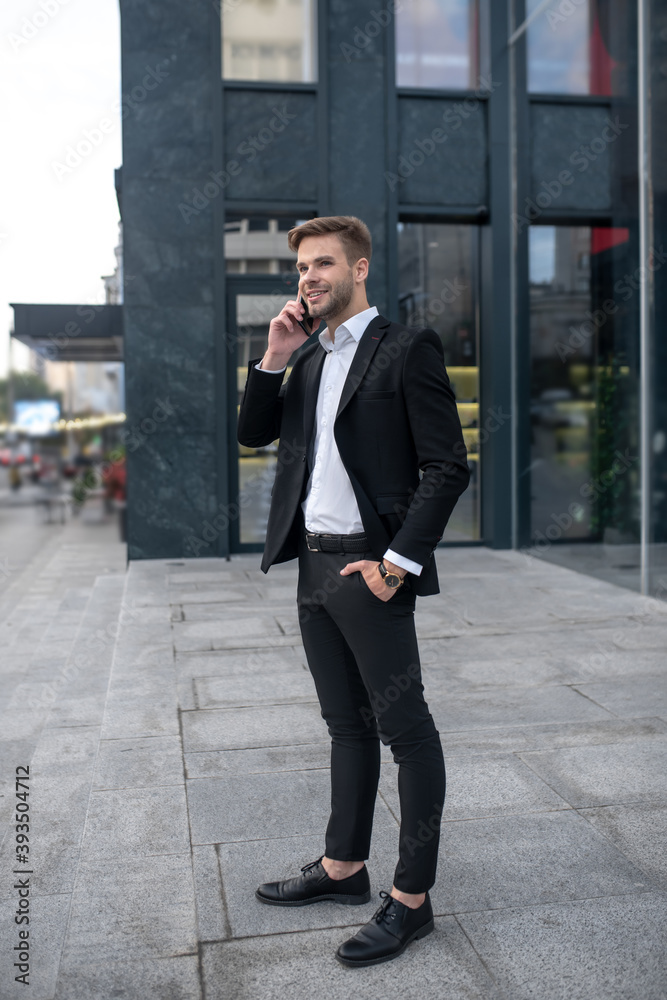 Young man in a black suit talking on the phone near business center Young man in a black suit talking on the phone near business center