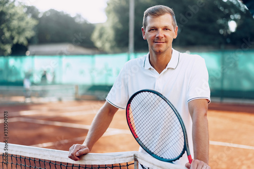Portrait of positive male tennis player with racket standing at clay court © fotofabrika