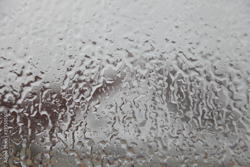 Icy rain, ice drops on outdoor glass surface on blurred house roof backdrop, abstract winter texture for background