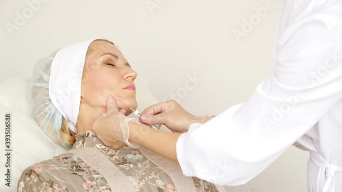 Doctor inserts a needle into a woman's face subcutaneously close-up. photo