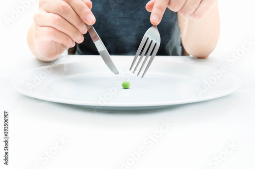Woman eating a small green pea using knife and fork. Extreme weight loss diet concept.