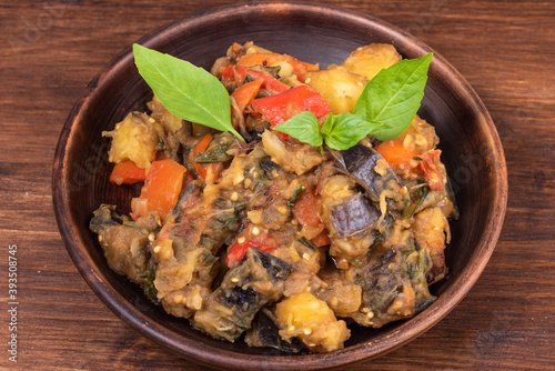 Italian vegetable stew with potatoes, eggplants, tomatoes, pepper in a rustic clay plate, decorated with fresh basil leaves on a woody background - Ciambotta, cianfotta in Neapolitan style.