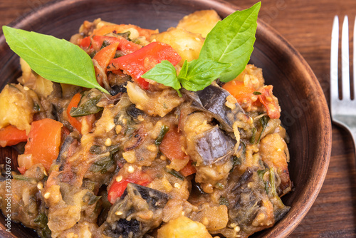 Italian vegetable stew with potatoes, eggplants, tomatoes, pepper in a rustic clay plate, decorated with fresh basil leaves on a woody background - Ciambotta, cianfotta in Neapolitan style. photo