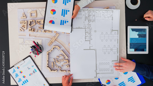 Top view of businesspeople team of architects with buildings prototype, gadgets and papers working at office table. Engineers brainstorming using modern device on copy space, flat lay concept