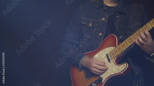 This is a close up shot of a fashionable man playing electric guitar on stage. This is a hand held shot in a contemporary setting with lots of energy. photo