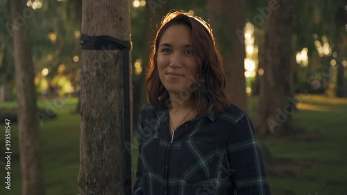 A beautiful young Asian woman is smiling in a park during the sunset. This clip is in slow motion, shot at 120p. photo