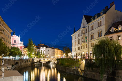 The promenade on the Ljubljanica river in the slovenian capital city Ljubljana with the Triple bridge and famous pink franciscan church at night