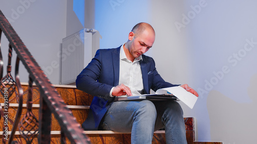 Overworked businessman reading raport after hours about deadline financial crisis sitting on stairscase in corporate building. Office executive checking graphs late finishing business deadline project photo