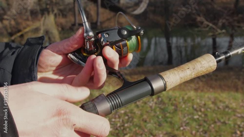 A man stands near a river and attaches a reel to a spinning rod