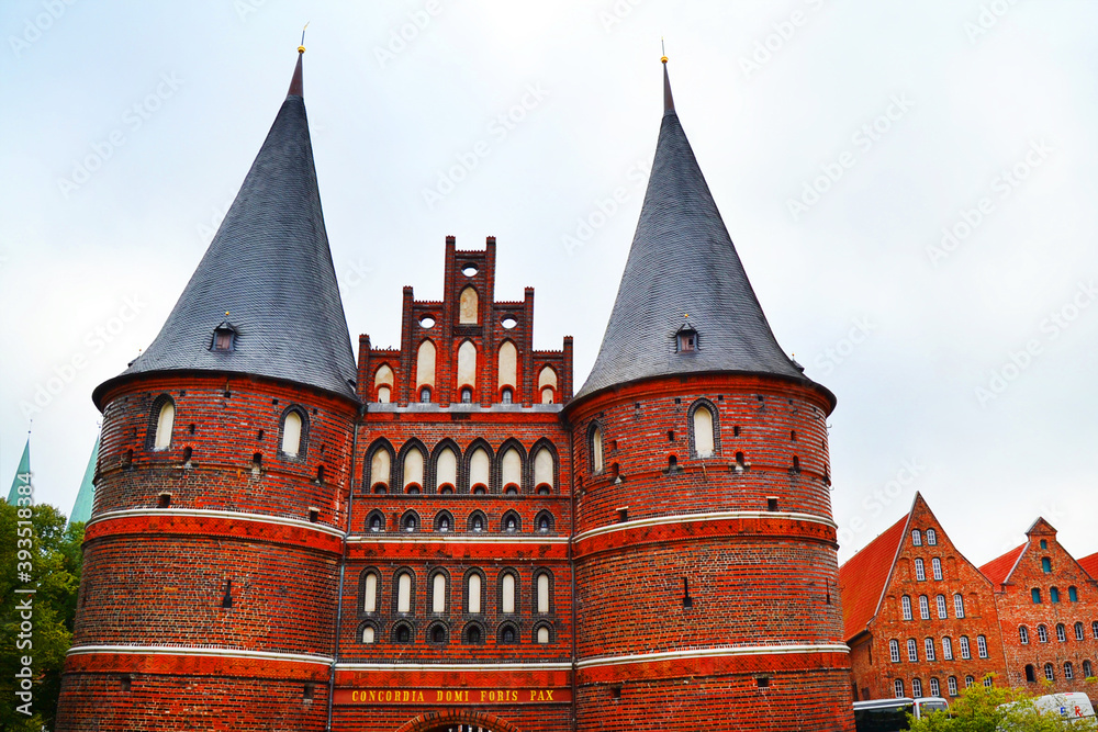 Beautiful view in Lubeck. Holstentor - medieval city gates with an inscription in Latin «Concordia Domi Foris Pax» (сonsent inside, peace outside) and brick buildings on a background.