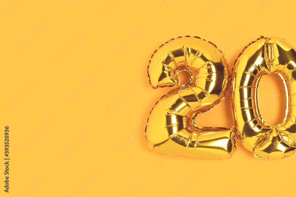 Number 20 golden balloons with copy space. Twenty years anniversary celebration minimalist concept on a yellow background.