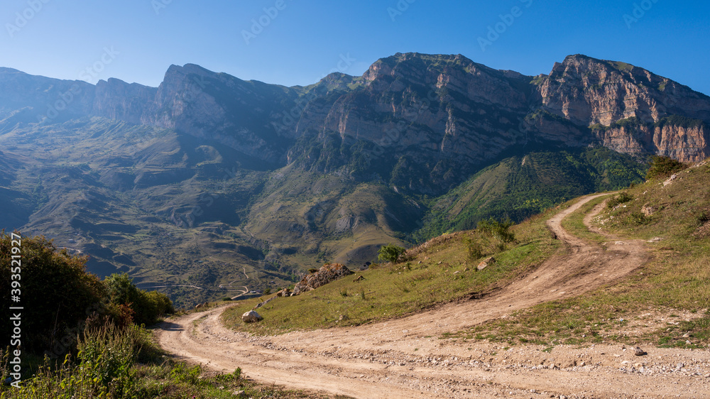 Obraz premium landscape in the mountains, field mountain road leading to a mountain village, against the background of mountains