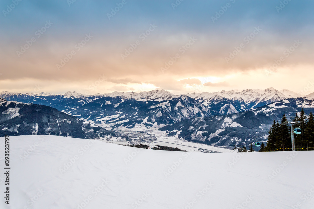 Zell am See at Zeller lake in winter. View from Schmittenhohe mountain, snowy slope of ski resort in the Alps mountains, Austria. Stunning landscape with snow and sunset sky near Kaprun
