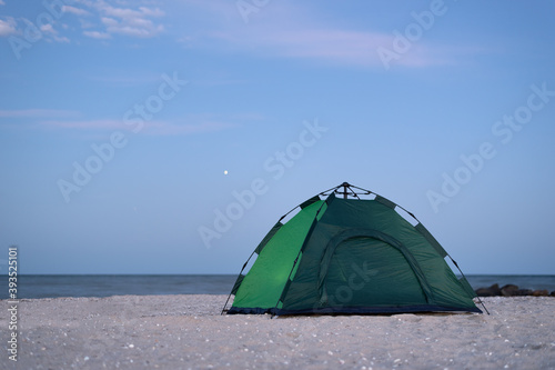 Green tent against blue sky and sea background. Camping on beach. Evening