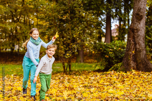 Two children are running on the park in fall leaves. Boy and girl are playing catch up along autumn path in the forest. Happy brother and sister are playing outdoors together. Activities in the fall.