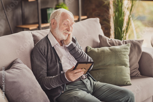 Photo of cute pensioner wear grey cardigan sitting couch looking photo frame good memories arm cheek indoors house flat