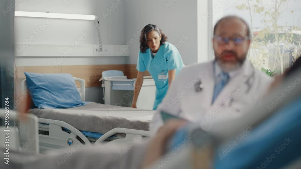Hospital Ward: Resting on Medical Bed Female Patient Listens to Experienced Latin Physician who Uses Digital Tablet Computer to Show, Explains Analysis Results. In Background Nurse Working Hospital Ward: Resting on Medical Bed Female Patient Listens to Experienced Latin Physician who Uses Digital Tablet Computer to Show, Explains Analysis Results. In Background Nurse Working