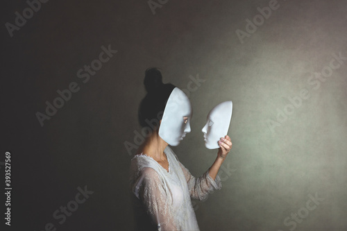 woman with mask looks at another mask of herself, concept of introspection photo