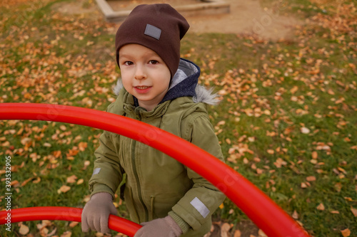 Young happy toddler boy stand on walk, autumn. Top view, shot through the red playground.