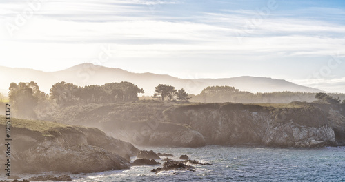 high key view of the misty and rocky tree-lined shore in Galicia