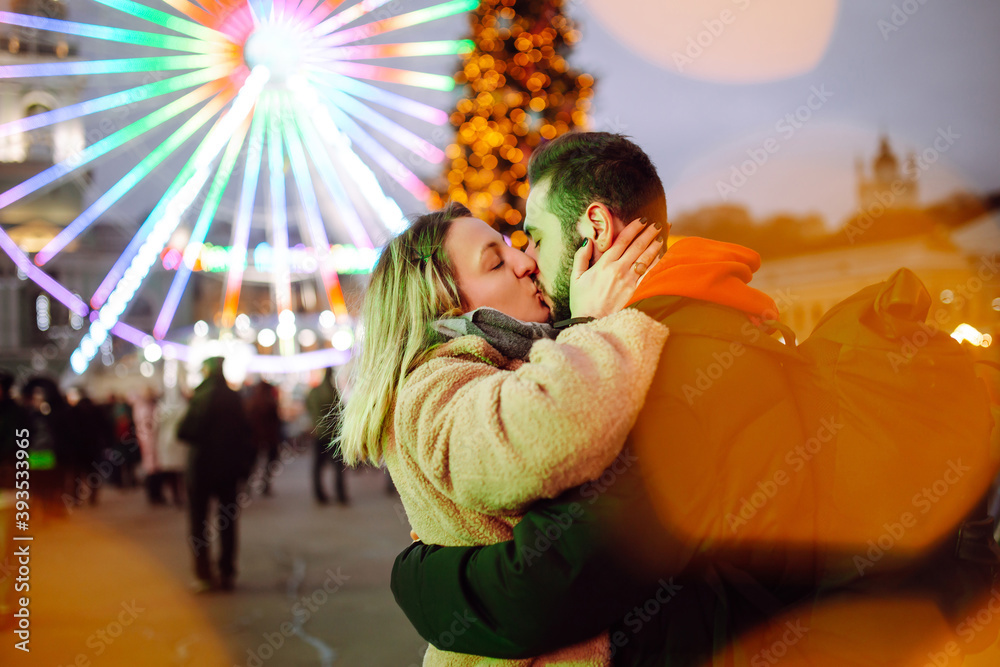 Happy couple in love walking on Christmas market at evening. Young woman and man at festive street market enjoying winter moments. Lights around. Christmas, New Year. Happy couple in love walking on Christmas market at evening. Young woman and man at festive street market enjoying winter moments. Lights around. Christmas, New Year.