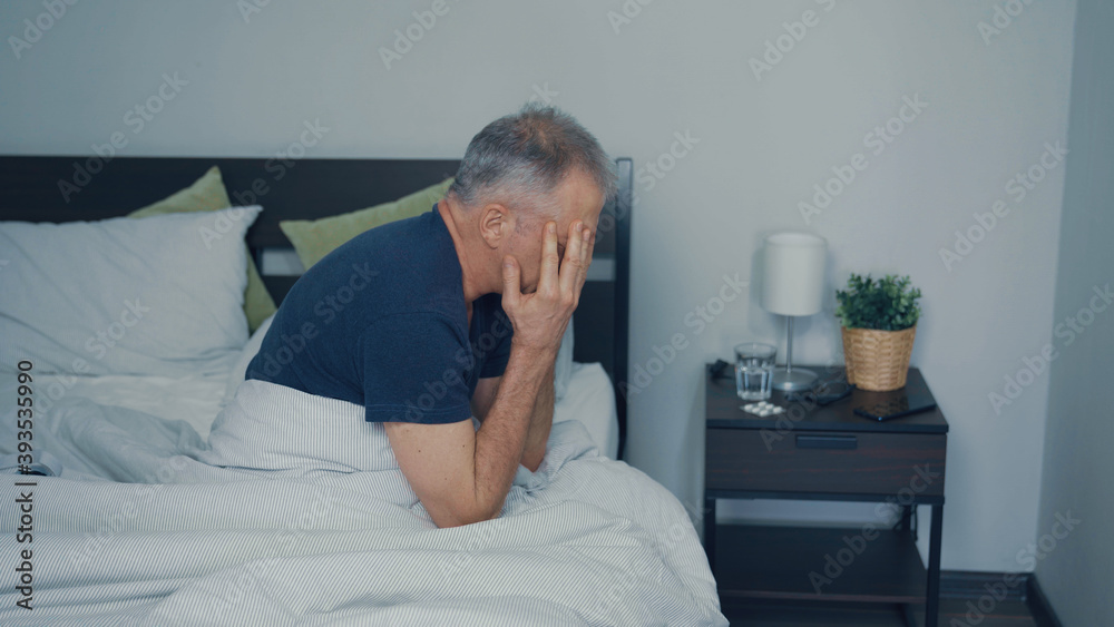 A middle-aged man suffers from a headache sitting on the bed. A middle-aged man suffers from a headache sitting on the bed.