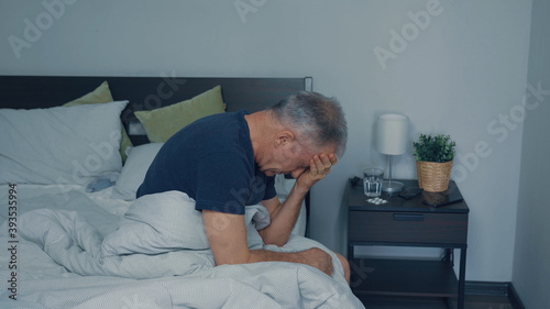 A middle-aged man suffers from a headache sitting on the bed.