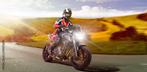 female motorcyclist riding motorbike on the country road accelerating while leaving the curve to overtake. motion blurring rural country side background. copy space to the right for your advertisement photo